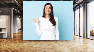 Young caucasian woman isolated on blue background pointing to the side to present a product Wall mural