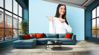 Young caucasian woman isolated on blue background pointing to the side to present a product Wall mural