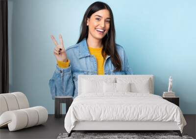 Young caucasian woman isolated on blue background smiling and showing victory sign Wall mural