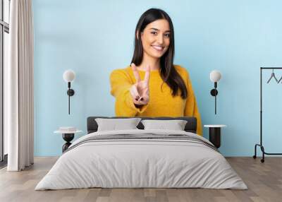 Young caucasian woman isolated on blue background smiling and showing victory sign Wall mural