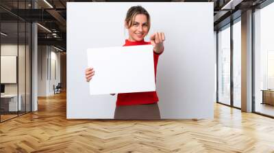 Young caucasian woman isolated on white background holding an empty placard and pointing to the front Wall mural