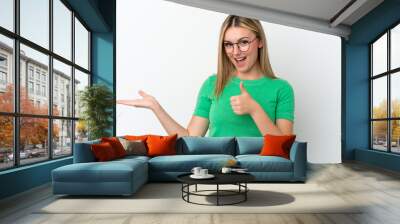 Young caucasian woman isolated on white background holding copyspace imaginary on the palm to insert an ad and with thumbs up Wall mural