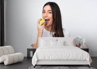 Young caucasian woman isolated on white background with a bottle of water and eating an apple Wall mural