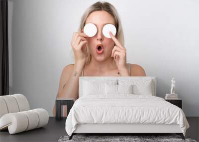 Young caucasian woman isolated on white background with cotton pad for removing makeup from her face Wall mural