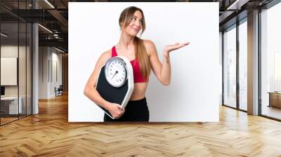 Young caucasian woman isolated on white background with weighing machine Wall mural