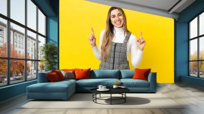 Young caucasian woman isolated on yellow background pointing up a great idea Wall mural