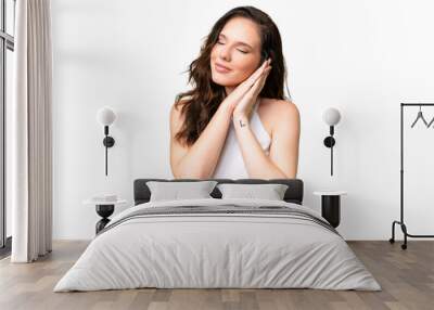 Young caucasian woman isolated over isolated background making sleep gesture in dorable expression Wall mural