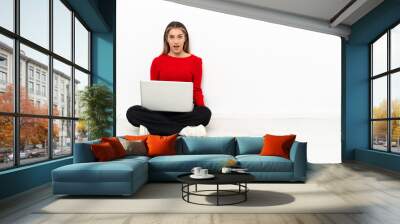 Young caucasian woman with a laptop sitting on the floor with surprise facial expression Wall mural