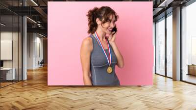 Young caucasian woman with medals isolated on pink background keeping a conversation with the mobile phone with someone Wall mural