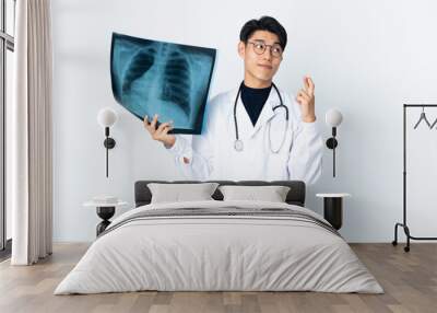 Young Chinese doctor man holding radiography isolated on white background with fingers crossing and wishing the best Wall mural