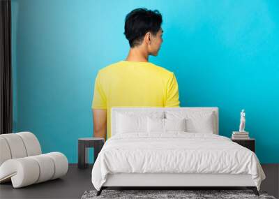 Young Chinese man isolated on blue background in back position and looking side Wall mural