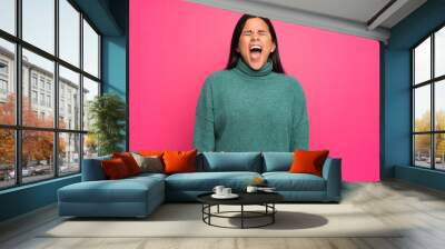 Young Colombian girl with green sweater shouting to the front with mouth wide open Wall mural