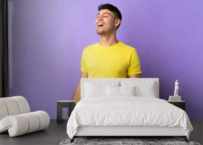 Young Colombian man isolated on purple background laughing Wall mural