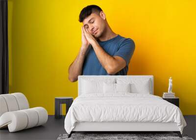 Young Colombian man isolated on yellow background making sleep gesture in dorable expression Wall mural