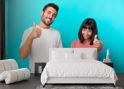 Young couple isolated on blue background giving a thumbs up gesture because something good has happened Wall mural