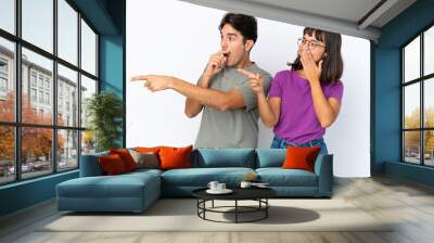 Young couple isolated on isolated white background pointing finger to the side with a surprised face Wall mural