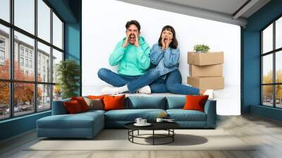 Young couple making a move while picking up a box full of things sitting on the floor isolated on white background shouting and announcing something Wall mural