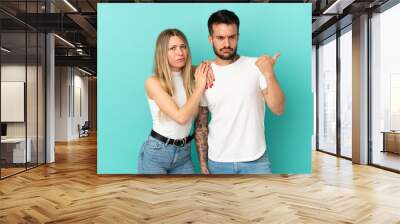 Young couple over isolated blue background frustrated and pointing finger to the side Wall mural