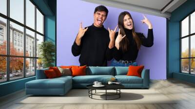 Young couple over isolated purple background making rock gesture Wall mural