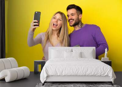 Young couple over isolated yellow background making a selfie with the mobile Wall mural