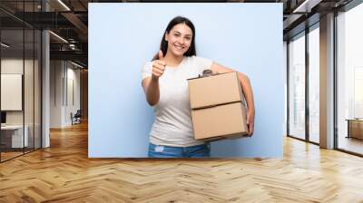 Young delivery woman over blue brick wall with thumbs up because something good has happened Wall mural