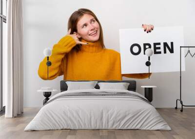 Young English woman isolated on white background holding a placard with text OPEN and doing phone gesture Wall mural