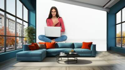 Young French girl sitting on the floor with her laptop pointing to the side to present a product Wall mural