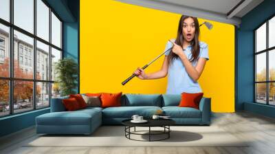 Young golfer woman over isolated yellow wall surprised and pointing side Wall mural