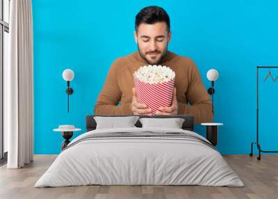 Young handsome man holding a big bucket of popcorns Wall mural