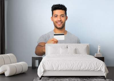 Young handsome man over isolated background holding a credit card Wall mural