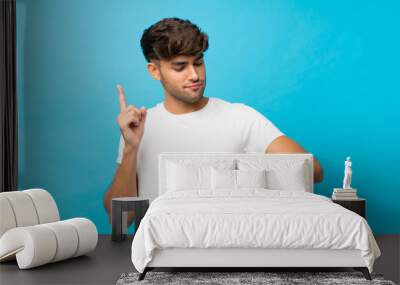 Young handsome man over isolated blue background looking at the hand watch Wall mural