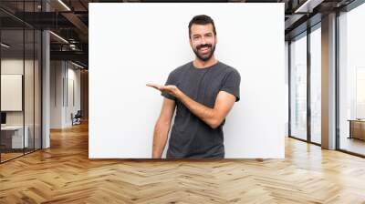 Young handsome man over isolated white background presenting an idea while looking smiling towards Wall mural