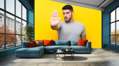 Young handsome man over isolated yellow background making stop gesture with her hand Wall mural