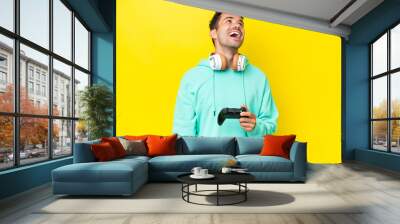 Young handsome man playing with a video game controller over isolated wall laughing Wall mural