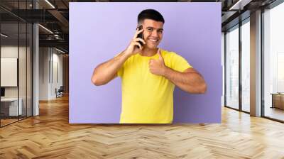 Young handsome man using mobile phone over isolated purple background giving a thumbs up gesture Wall mural