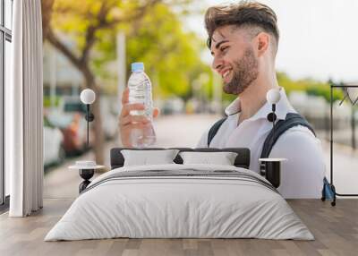 Young handsome man with a bottle of water at outdoors with happy expression Wall mural