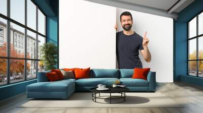 Young handsome man with beard holding a big empty placard showing and lifting a finger in sign of the best Wall mural