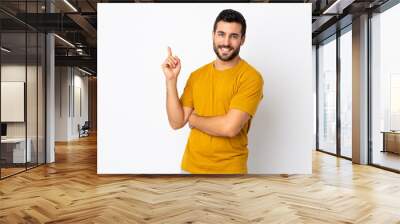 Young handsome man with beard isolated on white background happy and pointing up Wall mural