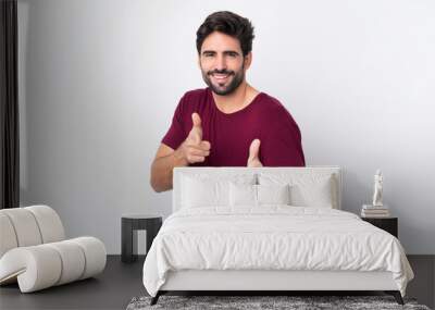 Young handsome man with beard over isolated white background pointing to the front and smiling Wall mural