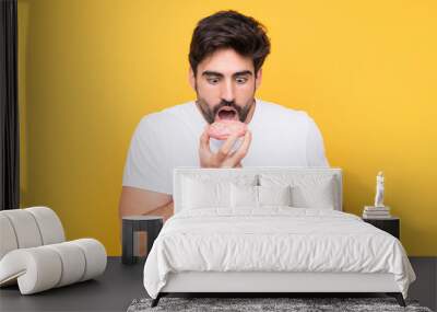 Young handsome man with beard over isolated yellow background eating a donut Wall mural