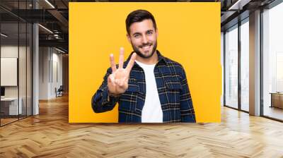 Young handsome man with beard over isolated yellow background happy and counting three with fingers Wall mural