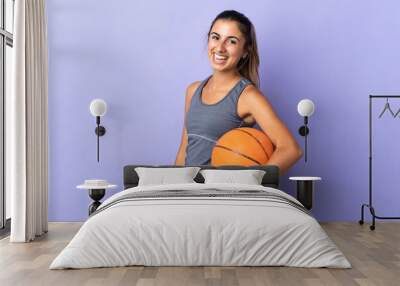 Young hispanic woman over isolated purple background playing basketball Wall mural