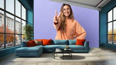 Young hispanic woman over isolated purple background smiling and showing victory sign Wall mural