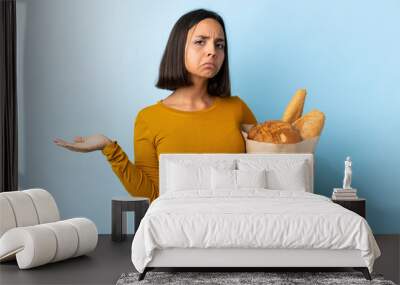 Young latin woman buying some breads isolated on blue background making doubts gesture Wall mural