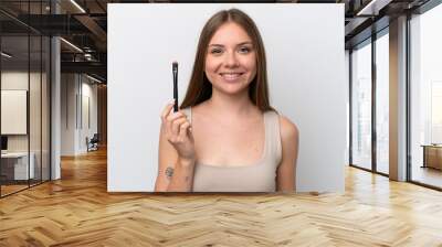 Young Lithuanian woman isolated on white background holding makeup brush and whit happy expression Wall mural