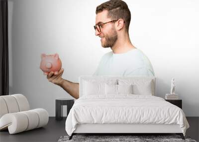 Young man holding a piggybank over isolated chroma key background with happy expression Wall mural