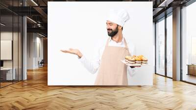 Young man holding muffin cake over isolated white background holding copyspace with two hands Wall mural