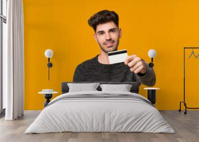 Young man over isolated background holding a credit card Wall mural