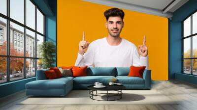 Young man over isolated orange background pointing up a great idea Wall mural