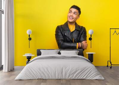 Young man over isolated yellow background looking up while smiling Wall mural